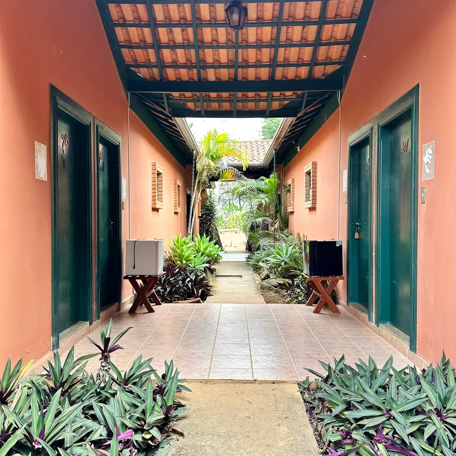 Corredor dos apartamentos, com portas verdes, telhado de madeira e jardim